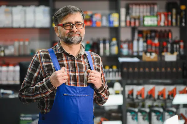 Mavi tulumlu, kendine güveni tam bir satıcının portresi. Pantolon askısı elinde. Bir oto yedek parça mağazasında duruyor.