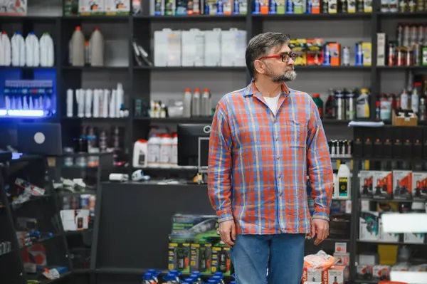 Bir oto yedek parça mağazasında kıdemli satıcı raflardaki ürünlere bakıyor, envanterleri kontrol ediyor ya da müşterilere yardım ediyor.