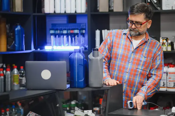 Satıcı kasada barkod tarayıcı kullanıyor, oto yedek parça mağazasında motor yağı ve diğer araba ürünleri satıyor.