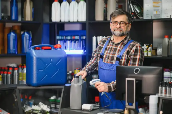 Kıdemli satıcı, otomobil parçaları mağazasında barkod tarayıcısıyla motor yağını tarıyor. Etrafı ürünlerle dolu.