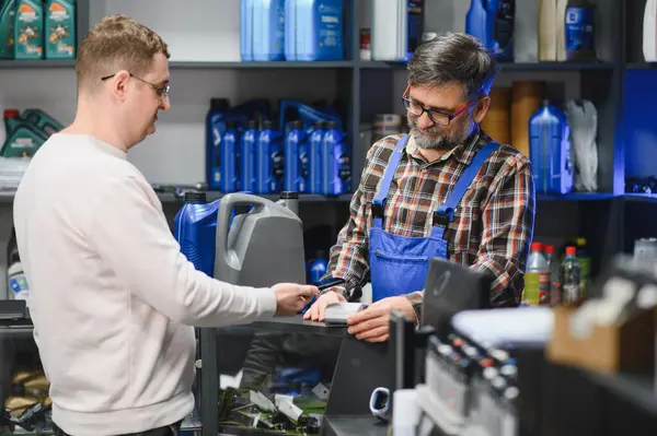 Tamirci, oto-gereç dükkanında müşterinin akıllı telefonuyla temas kuramadığı ödemeler yaparken duruş terminalini tutuyor.