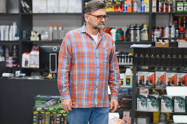 Oto yedek parça mağazasında çalışan kıdemli satıcı, raflardaki ürünleri kontrol eden, müşterilere otomotiv ihtiyaçları konusunda yardımcı olan