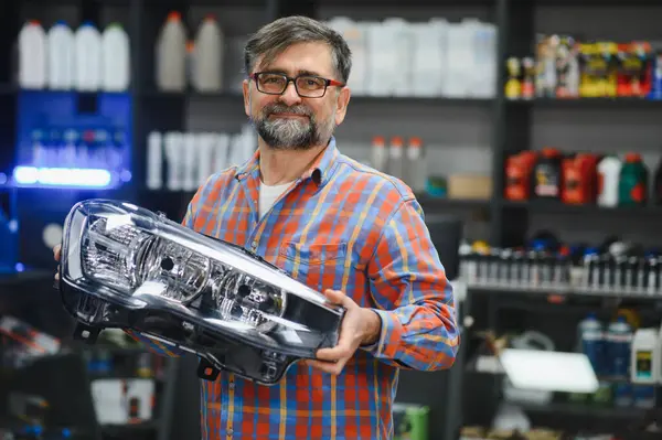 Oto yedek parça mağazasında yeni bir araba farını gösteren olgun bir satıcı, araç aydınlatma ihtiyaçları için uzman tavsiyesi ve çözümler sunuyor