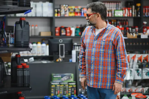 Tamirci, otomobil yedek parça deposundan motor yağı seçerek, en uygun araç bakımı ve onarımı için raflardaki çeşitli seçenekleri inceliyor