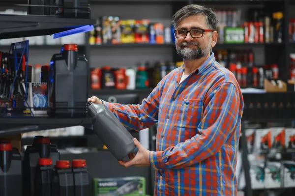 Bir oto yedek parça mağazasında satış elemanı motor yağını tutuyor ve kontrol ediyor. Müşterisi için doğru ürünü seçiyor.