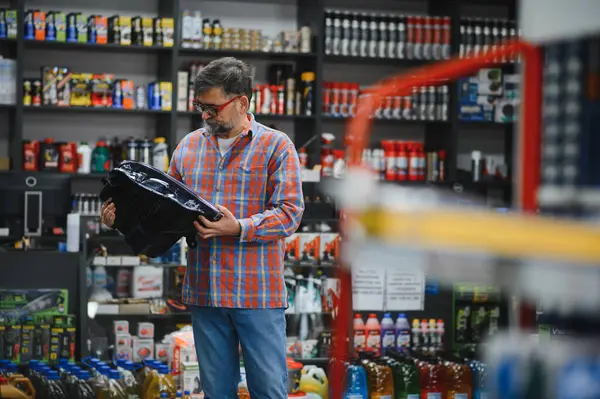 Tamirci bir oto yedek parça mağazasından araba parçası seçiyor, yedek parça tutuyor ve kalitesini kontrol ediyor.