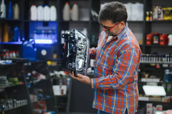 Tecrübeli bir tamirci iyi stoklanmış bir oto yedek parça mağazasında araba farlarını dikkatlice inceleyerek kalite ve uyum sağlıyor.