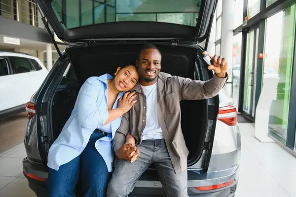 Yeni araba anahtarlarını açık sandıkta otururken gösteren heyecanlı çift, araba galerisinde alışverişlerini kutluyor.