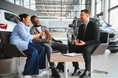 Heyecanlı çift yeni araba anahtarlarını profesyonel bir satıcıdan alıyor. Satıcıdaki alışverişi sonuçlandırıyorlar.