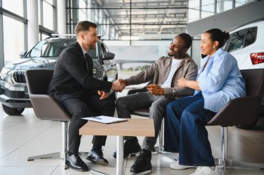 Satıcı birkaç müşteriyle el sıkışıyor, modern bir galeride araba alımını sonuçlandırıyor, el sıkışarak işi bitiriyor.