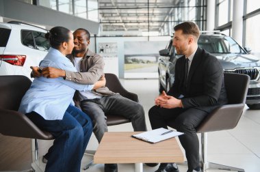 Galerideki başarılı araba alımından sonra kucaklaşan heyecanlı çift profesyonel satıcıyla evrak işlerini hallediyor.