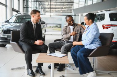 Gülümseyen Afro-Amerikan çifti, araba galerisindeki dost bir satıcıdan yeni araba anahtarlarını almaktan mutluluk duyuyorlar.