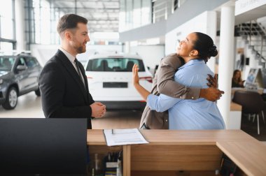 Yeni araba aldıktan sonra bayilikte kucaklaşan heyecanlı çift, satış elemanlarıyla yaptıkları başarıyı kutluyor.