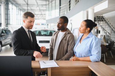 Araba satıcısı Afrikalı Amerikalı bir çifte sözleşmeyi açıklarken modern bir bayiden yeni bir araba alma potansiyeli var.