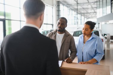 Araba satıcısı, modern bir galeride yeni bir araç seçerken Afro-Amerikan bir çifte yardımcı oluyor. Seçenekleri ve finansal detayları tartışıyorlar.