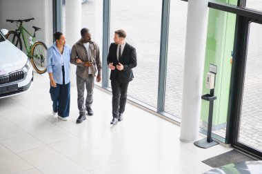 Otomobil galerisinde yürüyen araba satıcısı, araba satın alma seçenekleri ve tercihleri hakkında birkaç kişiyle sohbet ediyor.