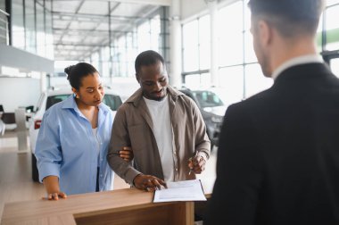 Afro-Amerikalı çift, profesyonel pazarlamacının da yardımıyla galeride yeni araba satın alma sözleşmesi imzalıyor.