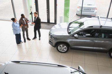 Araba satıcısı, modern bir araba galerisinde Afro-Amerikan bir çifte yeni bir araba sunuyor. Satın alma seçeneklerini tartışıyorlar.