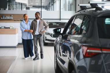 Afro-Amerikalı çift el ele tutuşup galeride yeni arabalarını seçiyorlar ve satış temsilcisiyle konuşuyorlar.