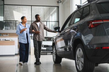 Afro-Amerikalı çift galeride yeni bir arabayı inceliyor, özellikleri tartışıyor ve karar veriyorlar.