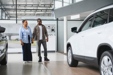 Canlı bir galeride yeni bir araba için seçenekleri değerlendirirken, satın alma deneyiminin tadını çıkaran Afrikalı Amerikalı çift el ele tutuşuyor.