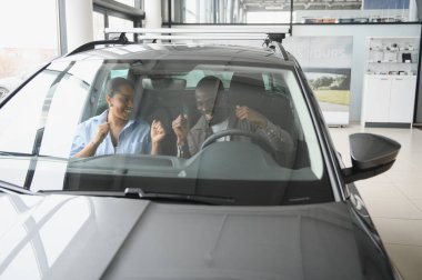 Mutlu çift yeni arabalarının içinde tezahürat yapıyor, satın almalarının heyecan verici başarısını gülümseme ve neşeyle kutluyorlar.