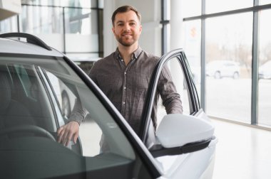 Mutlu müşteri yeni bir arabanın kapısını açıyor ve modern bir galeride bir sonraki aracını seçiyor.
