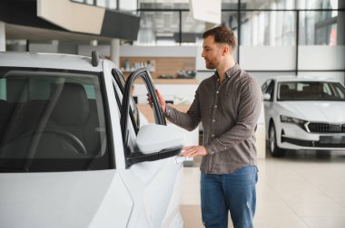 Satıcıda yeni bir beyaz arabayı inceleyen bir adam. Satın almadan önce kapıyı açıp içeriyi kontrol ediyor.