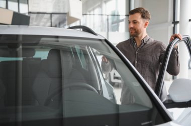 Gülümseyen müşteri yeni bir arabanın kapısını açıyor, gelecekteki aracını galeride seçiyor.