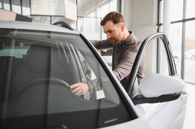 Mutlu müşteri, yeni bir arabanın içini incelemekten zevk alıyor. Gösterişli bir galeride direksiyona güvenle dokunuyor.