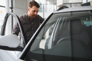 Otomobil galerisinde aracın içini inceleyen adam, yeni otomobil satın alma konusunda karar veriyor.