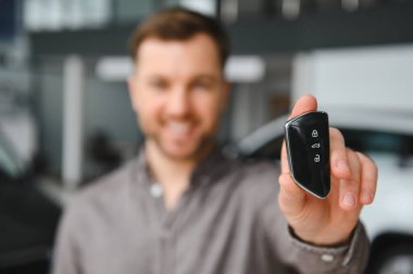Gülümseyen müşteri, galeride otomobil satın alırken yeni bir araba anahtarını gururla sergiliyor.