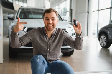 Araba anahtarlarını gösteren ve galeride başarılı bir alışveriş yaptıktan sonra yeni aracını gösteren heyecanlı adam.