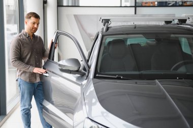 Müşteri araba galerisindeki yeni gri cipi inceliyor, kapıyı açıyor ve test sürüşüne hazırlanıyor.