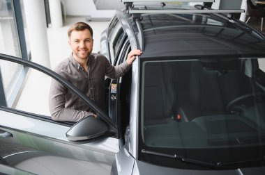 Mutlu adam galeride yeni bir araba alma tecrübesinden zevk alıyor. Arabanın tavanına dokunuyor ve kapıyı açıyor.