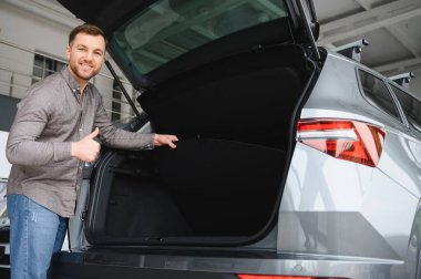 Bir galeri galerisinde yeni bir arabanın bagajını incelerken mutlu adam, seçiminden memnun.