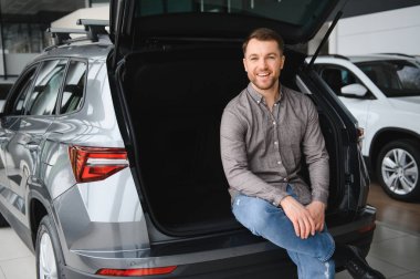 Mutlu müşteri açık araba bagajında oturuyor, boşluğu kontrol ediyor ve gelecekteki seyahatlerini galeride hayal ediyor.