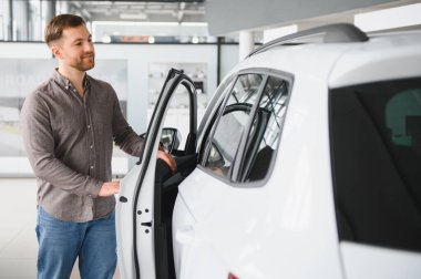 Müşteri gösterişli beyaz bir arabanın içini inceliyor, modern bir araba galerisinde seçenekleri incelerken kapıyı açıyor.