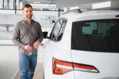 Parlak bir galeride yeni araba alımını kutlayan mutlu bir adam. Mülkiyet ve yatırım heyecanının tadını çıkarıyor.