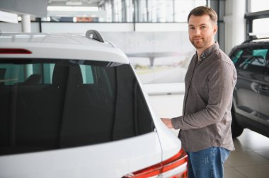 Otomobil galerisinde yeni beyaz bir arabanın bagajını açan adam, gelecekteki maceralar için modern bir araç almaya karar veriyor.