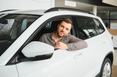 Galeride yeni bir SUV 'un içinde oturan yakışıklı adam, arabanın camından sarkıyor.