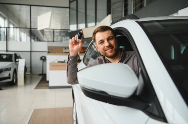 Gülümseyen müşteri yeni araba anahtarlarını gururla tutarken bir galeride modern bir araçta otururken heyecan ve memnuniyet saçıyor.