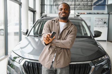 Gururlu Afrikalı Amerikalı adam yeni arabasının anahtarlarını galeride sergiliyor. Mutluluk ve heyecan saçıyor.