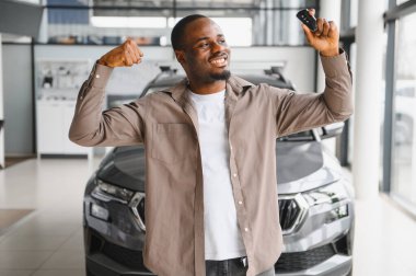 Heyecanlı bir adam kaslarını esnetiyor, arabanın anahtarlarını tutuyor galeride yeni bir araba almayı kutluyor.