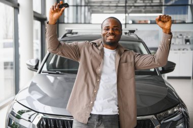 Heyecanlı adam yeni araba almayı kutluyor, anahtarlar elinde ve galeride zafer için silah kaldırıyor.