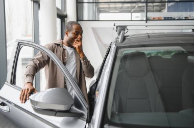 Yeni bir araba almayı düşünen düşünceli bir adam, otomobil galerisinde araç özelliklerini inceleyen biri.