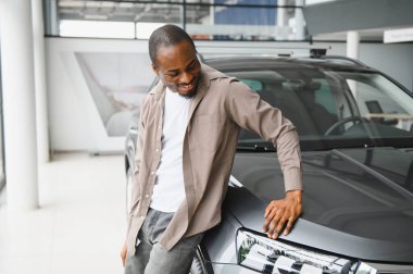 Gülümseyen müşteri, araba galerisindeki yeni alımına hayran kaldı. Hayalindeki aracı elde etme anının tadını çıkarıyor.