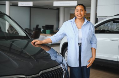 Afro-Amerikalı bir kadın galeride yeni bir arabanın kaputuna dokunuyor, heyecanla araba satın alma sürecine giriyor.