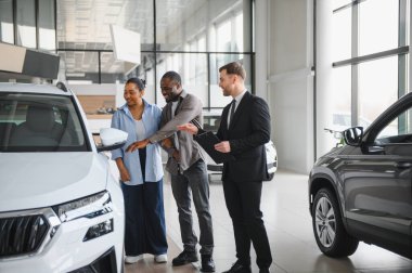 Araba satıcısı, Afrika kökenli Amerikalı çifte yeni arazi aracı gösteriyor. Özellikleri ve finansman seçeneklerini tartışıyorlar.