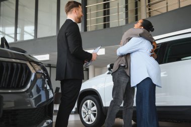 Araba satıcısı, Afro-Amerikan bir çiftin galeriden yeni araba almasına yardım ederken sözleşmeyi tutuyor.